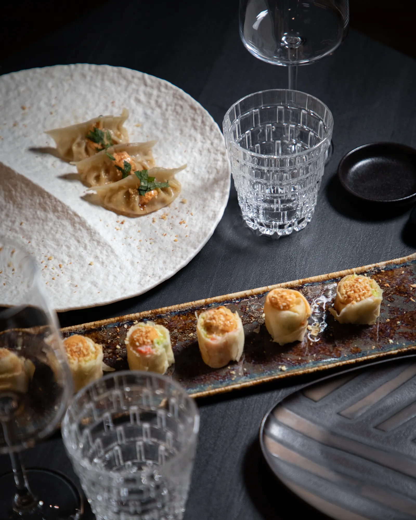 Gyoza e bocconcini su tavolo scuro con calici di vino da Konoha Sushi
