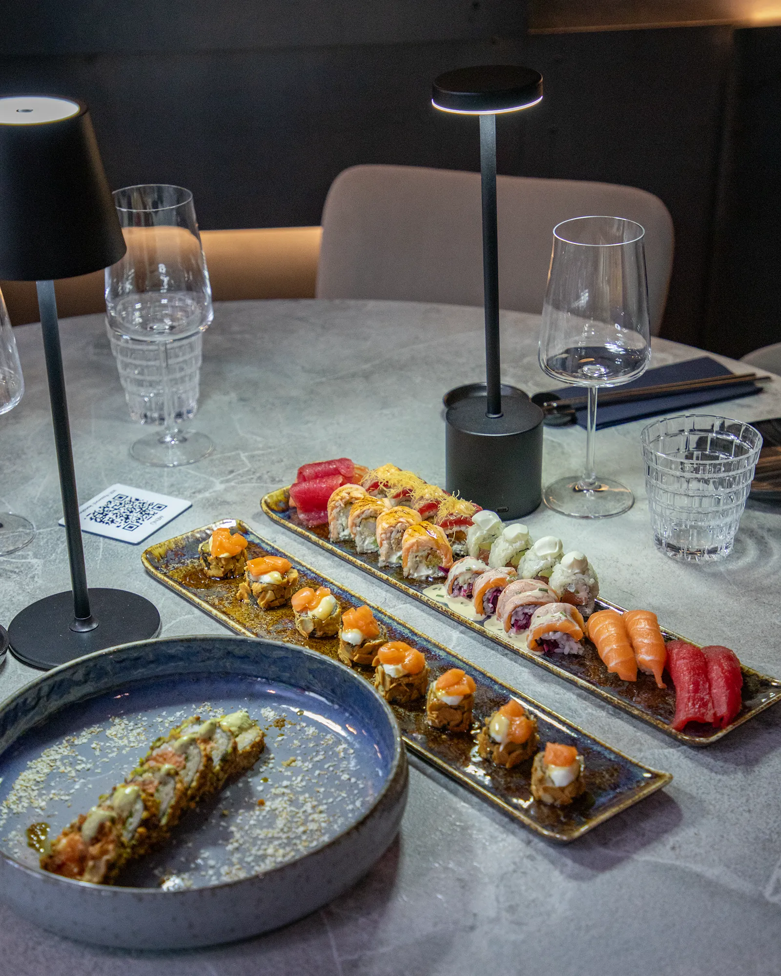 Tavolo di Konoha Sushi apparecchiato con piatti lunghi di nigiri e uramaki e calici